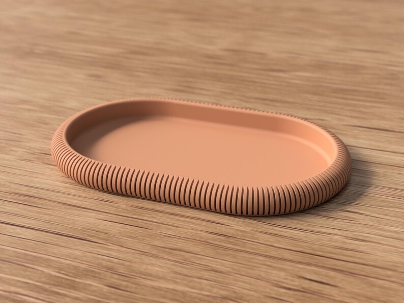 Puede incluir: Una bandeja ovalada de color melocot&oacute;n con un borde acanalado. La bandeja est&aacute; hecha de un material s&oacute;lido y se encuentra sobre una superficie de madera. El dise&ntilde;o es simple y moderno, adecuado para varios usos.
