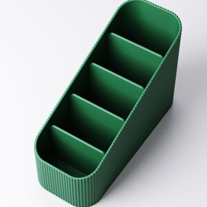 May include: A green desk organizer with five compartments. The organizer has a ribbed texture on the sides and a smooth interior. The compartments are separated by vertical dividers, and the overall shape is rectangular with rounded corners.