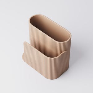 Pu&ograve; includere: Un organizer da scrivania beige e a coste. L'organizer ha un vano principale di forma ovale e una tasca anteriore curva pi&ugrave; piccola. Le linee verticali creano una superficie strutturata. Il design &egrave; minimalista e funzionale.