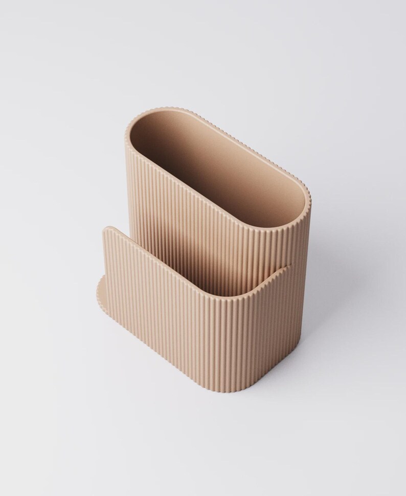 Pu&ograve; includere: Un organizer da scrivania beige e a coste. L'organizer ha un vano principale di forma ovale e una tasca anteriore curva pi&ugrave; piccola. Le linee verticali creano una superficie strutturata. Il design &egrave; minimalista e funzionale.