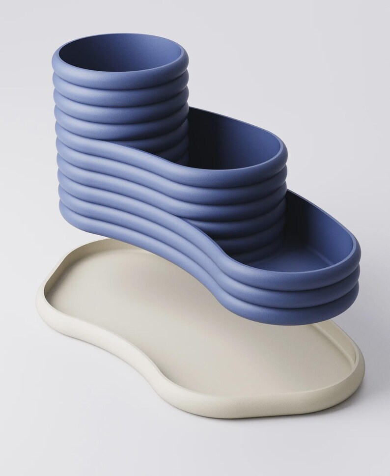 May include: A modern, abstract sculpture in shades of blue and off-white. The blue element features a tiered, wavy design with a cylindrical top and a curved, open section. It rests above a smooth, off-white, organically shaped tray.