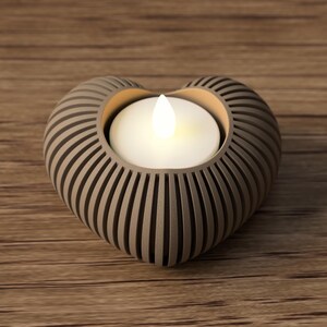 May include: A heart-shaped candle holder with a lit white candle. The holder is a light brown color with vertical grooves. The candle holder sits on a wooden surface.