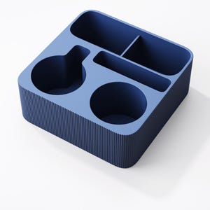 May include: A square blue desk organizer featuring a ribbed exterior texture. The interior is divided into five distinct compartments of varying shapes and sizes, including two circular sections, one long rectangular slot, and two smaller square spaces.