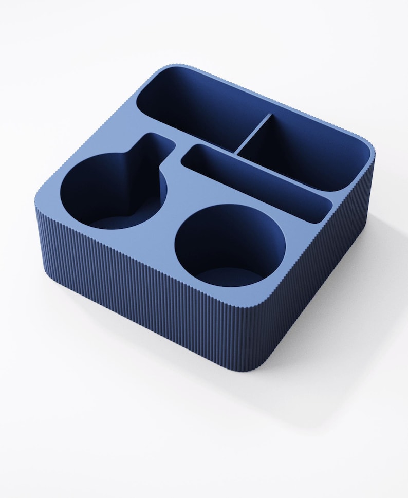May include: A square blue desk organizer featuring a ribbed exterior texture. The interior is divided into five distinct compartments of varying shapes and sizes, including two circular sections, one long rectangular slot, and two smaller square spaces.