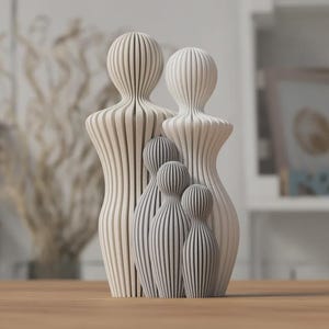 Puede incluir: Un conjunto de esculturas familiares con un dise&ntilde;o moderno. El conjunto incluye dos figuras grandes y tres m&aacute;s peque&ntilde;as, todas en una paleta de colores neutros de blanco y gris. Las figuras tienen un patr&oacute;n de rayas verticales.