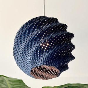 May include: A spherical pendant light fitting with a dark blue, textured, 3D-printed lattice shell. The structure features a swirling, wave-like pattern with small perforations that allow light to pass through, suspended by a white cord.