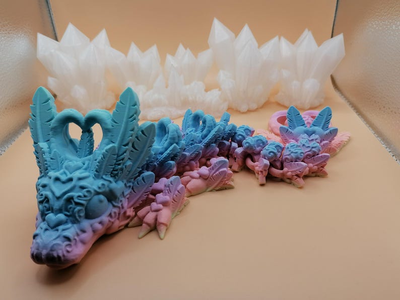 May include: A detailed image of a fantasy dragon sculpture in shades of blue and pink, with intricate feather and heart details. The dragon is positioned in front of several white crystal formations, creating a whimsical and artistic display.