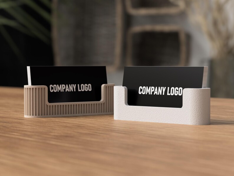 May include: Two business card holders on a wooden surface. Each holder is a different design, one with vertical ridges and the other with a smooth, rounded shape. Both hold black cards with the text "COMPANY LOGO" in white.