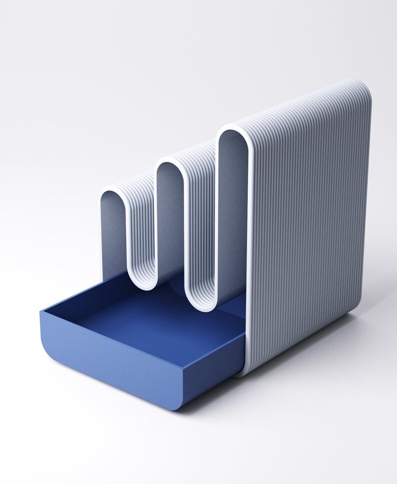 May include: A modern, minimalist desk organizer in shades of blue and white. The design features a wavy, vertical structure with a pull-out drawer. The exterior has a ribbed texture, and the drawer is a solid, deep blue.