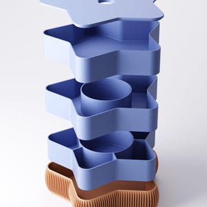 May include: A stackable storage unit with a star shape. The unit is composed of several light blue trays and a star-shaped lid. The base is a contrasting tan color with vertical ridges. The design is modern and geometric.