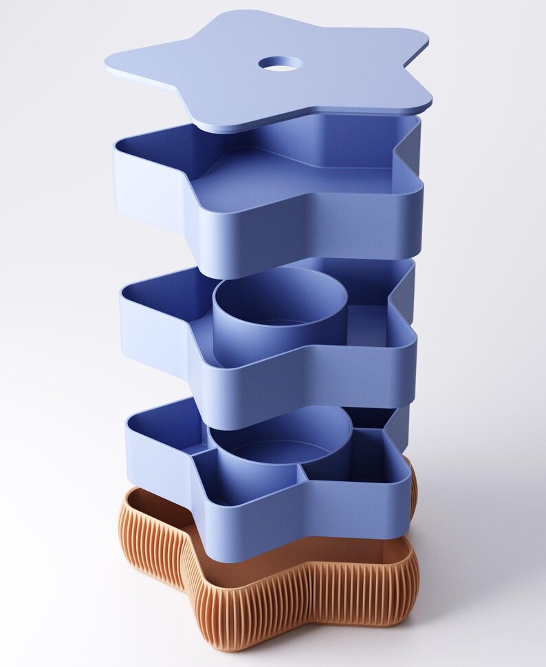 May include: A stackable storage unit with a star shape. The unit is composed of several light blue trays and a star-shaped lid. The base is a contrasting tan color with vertical ridges. The design is modern and geometric.