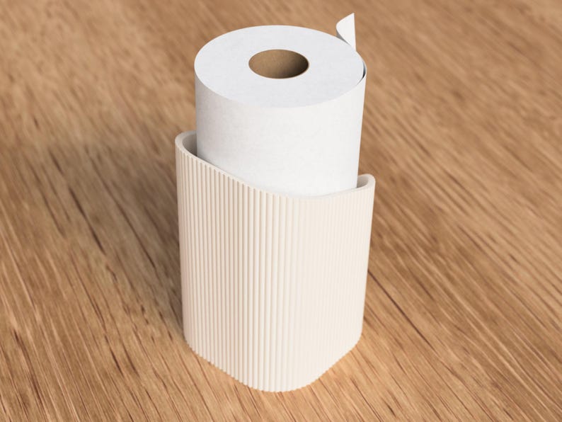 Op de afbeelding: Een witte rol toiletpapier staat in een beige, geribbelde houder. De houder heeft een gebogen ontwerp en is gemaakt van een solide materiaal. De achtergrond is een lichtbruin houten oppervlak.
