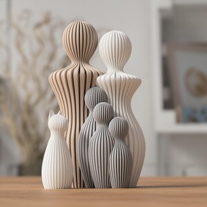 Puede incluir: Colecci&oacute;n de figuras de madera de varios tama&ntilde;os y colores. Las figuras incluyen un gato, dos figuras altas y varias figuras m&aacute;s peque&ntilde;as. Las figuras est&aacute;n hechas de madera marr&oacute;n claro, blanca y gris, con un dise&ntilde;o a rayas.