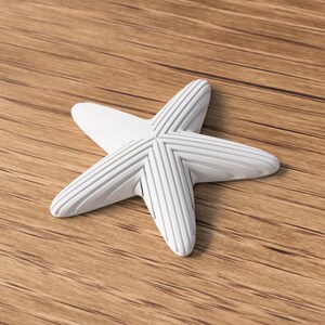 May include: A white starfish with textured, ridged detailing. The five-pointed sea creature is resting on a wooden surface with a natural grain pattern. The starfish is a decorative item, possibly for coastal or nautical themed decor.