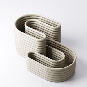 May include: A contemporary sculpture in a pale grey hue. The artwork presents a continuous, flowing design composed of stacked, curved shapes. The surface is textured with ridges, enhancing the minimalist aesthetic. The sculpture is suitable for interior decor.