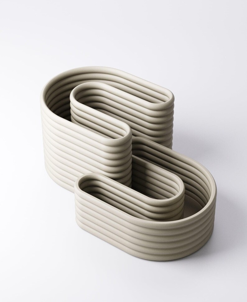 May include: A contemporary sculpture in a pale grey hue. The artwork presents a continuous, flowing design composed of stacked, curved shapes. The surface is textured with ridges, enhancing the minimalist aesthetic. The sculpture is suitable for interior decor.