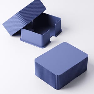 May include: A set of three matching blue-purple desk organizers. The set includes a rectangular box with a lid, and a container with a curved opening. The box and lid have a ribbed texture, while the container has a smooth surface.