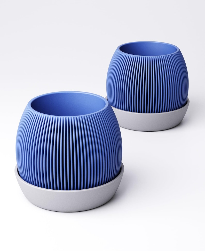 May include: Two blue, ribbed planters with a gray base are displayed against a white background. The planters have a rounded shape with vertical lines, creating a textured effect. The interior of the planters is a solid blue color.