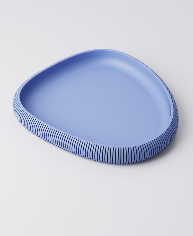 Puede incluir: Una bandeja azul claro de forma org&aacute;nica con borde acanalado. La bandeja tiene un interior liso y un borde texturizado con l&iacute;neas verticales. El dise&ntilde;o es minimalista y moderno, adecuado para servir o exhibir.