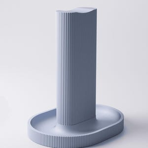 May include: A light blue vertical stand with a ribbed texture on the exterior. The object features a tall, rectangular central column with a concave top, mounted onto an oval-shaped base that also displays a consistent vertical ribbed pattern.
