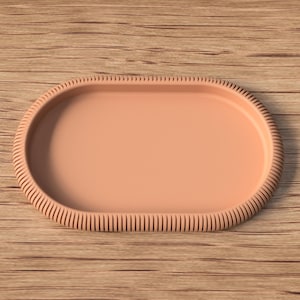 Puede incluir: Una bandeja ovalada de color melocot&oacute;n con un borde texturizado y acanalado. La bandeja est&aacute; sobre una superficie de madera. El dise&ntilde;o de la bandeja es simple y elegante, adecuada para servir o exhibir.
