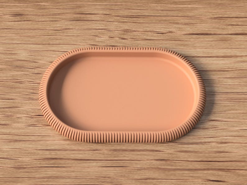 Puede incluir: Una bandeja ovalada de color melocot&oacute;n con un borde texturizado y acanalado. La bandeja est&aacute; sobre una superficie de madera. El dise&ntilde;o de la bandeja es simple y elegante, adecuada para servir o exhibir.