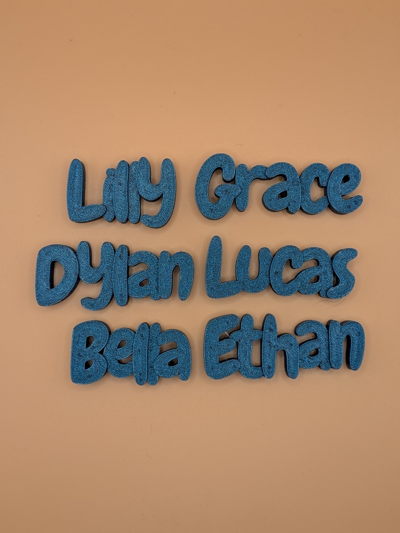 May include: Six teal wooden name cutouts: Lilly, Grace, Dylan, Lucas, Bella, and Ethan. The names are in a playful, rounded font, and are arranged in two rows on a peach-coloured background.