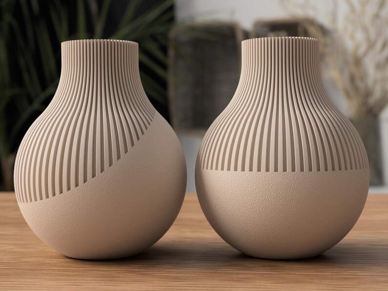 May include: Two beige decorative vases with a unique design. The upper portion of each vase features vertical, ridged detailing, while the lower half has a smooth, rounded surface. The vases are displayed on a wooden surface, suggesting a home decor theme.