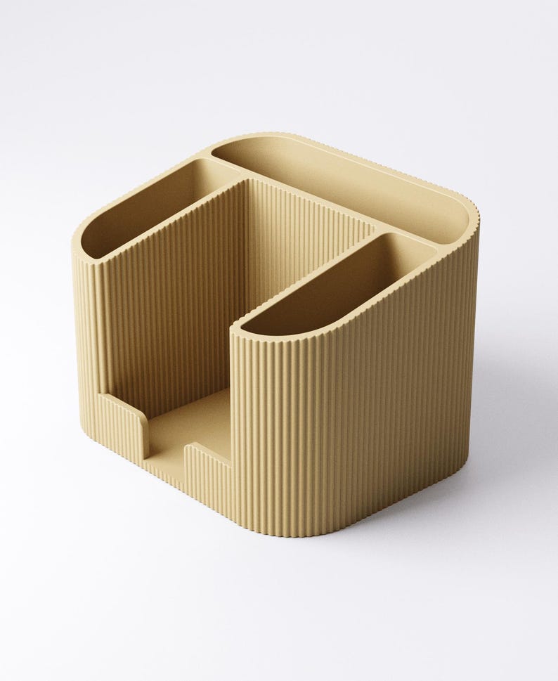 May include: A beige desk organizer with a ribbed texture. The organizer has multiple compartments of varying sizes, including slots for pens and a larger section for other supplies. The design is modern and minimalist, suitable for office or home use.