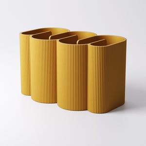 May include: Three mustard-yellow, ribbed, semi-circular containers with interior dividers. The containers are arranged in a row, with a minimalist design. The background is plain white.