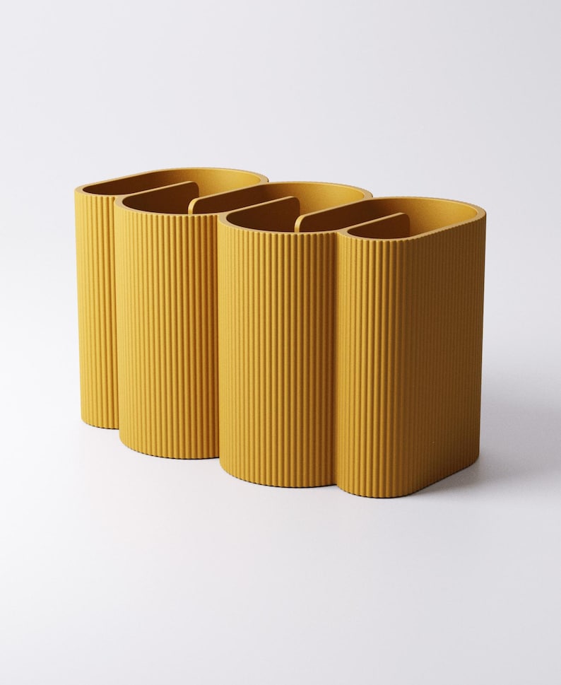 May include: Three mustard-yellow, ribbed, semi-circular containers with interior dividers. The containers are arranged in a row, with a minimalist design. The background is plain white.