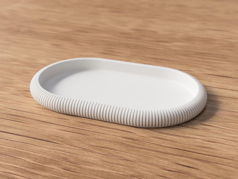 Puede incluir: Una bandeja blanca de forma ovalada con borde acanalado. La bandeja est&aacute; hecha de un material s&oacute;lido y se encuentra sobre una superficie de madera. El dise&ntilde;o es minimalista y moderno, adecuado para diversos usos.