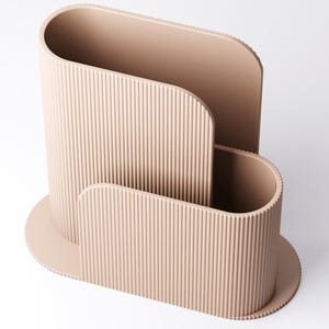 May include: A beige desk organiser with a ribbed texture. The organiser has a curved design with three compartments of varying sizes. The base is oval-shaped, and the overall aesthetic is modern and minimalist.