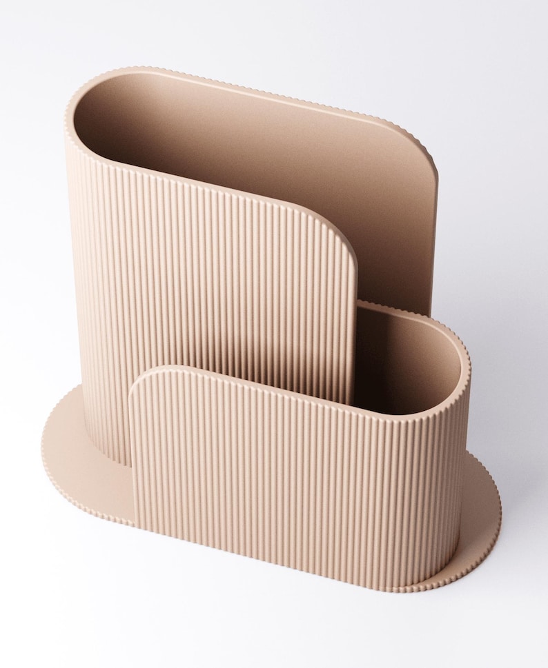 May include: A beige desk organiser with a ribbed texture. The organiser has a curved design with three compartments of varying sizes. The base is oval-shaped, and the overall aesthetic is modern and minimalist.