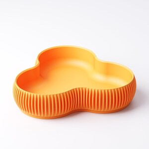 Pu&ograve; includere: Una ciotola arancione a forma di nuvola con esterno a coste. La ciotola ha un interno liscio e un design unico a tre lobi. Il colore &egrave; un arancione vibrante, che la rende un pezzo decorativo e funzionale per la casa.