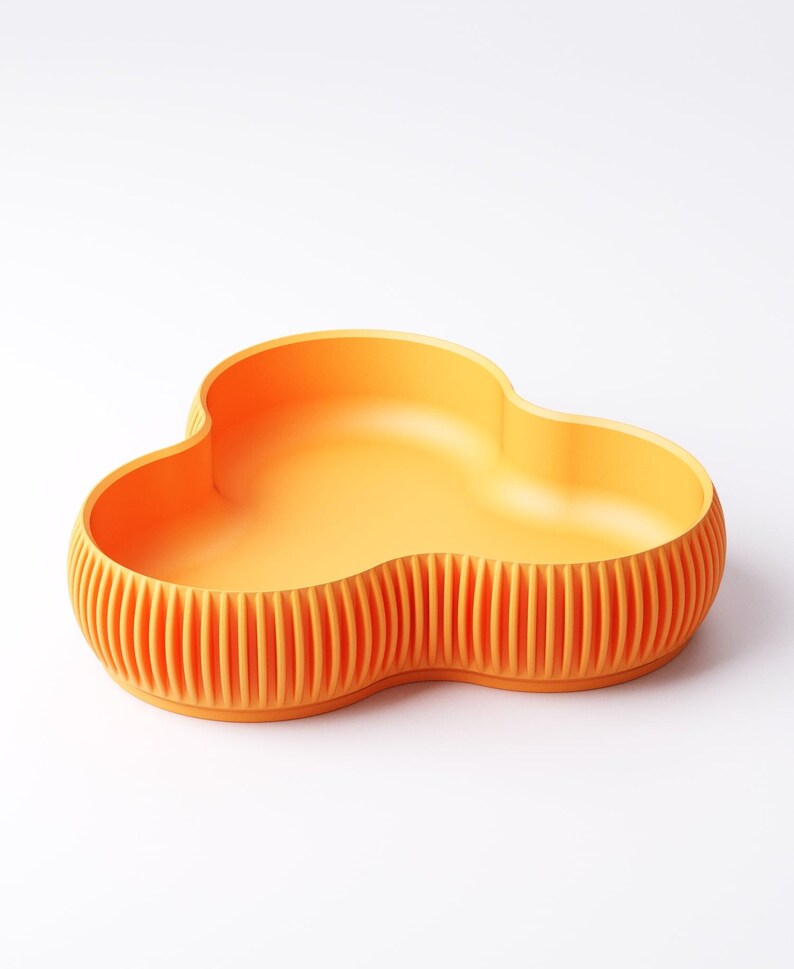 Pu&ograve; includere: Una ciotola arancione a forma di nuvola con esterno a coste. La ciotola ha un interno liscio e un design unico a tre lobi. Il colore &egrave; un arancione vibrante, che la rende un pezzo decorativo e funzionale per la casa.
