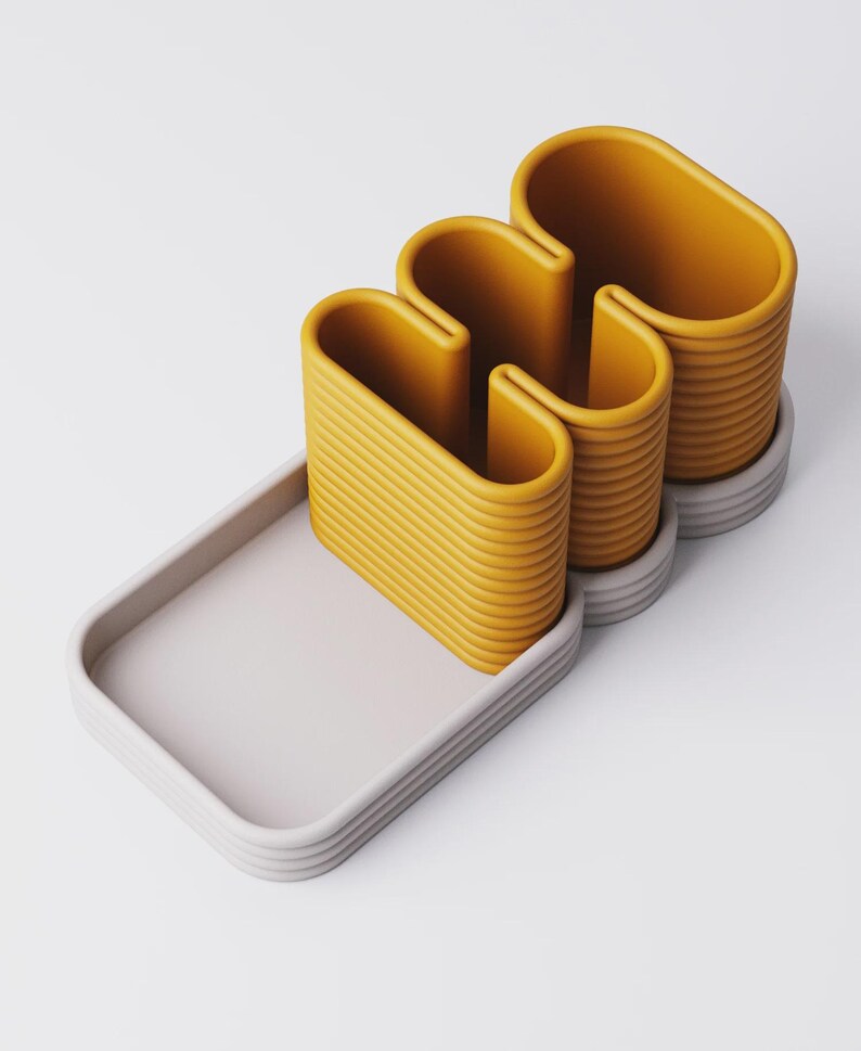 Puede incluir: Conjunto decorativo abstracto moderno. Presenta un objeto ondulado amarillo mostaza con textura acanalada, sobre una bandeja rectangular gris claro. El conjunto incluye una base a juego. Dise&ntilde;o minimalista y contempor&aacute;neo.