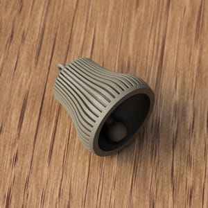 May include: A gray bell-shaped object with a rounded bottom and a small clapper inside. The bell has a series of vertical, curved lines on its exterior. The bell is resting on a wooden surface.