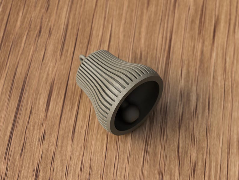 May include: A gray bell-shaped object with a rounded bottom and a small clapper inside. The bell has a series of vertical, curved lines on its exterior. The bell is resting on a wooden surface.