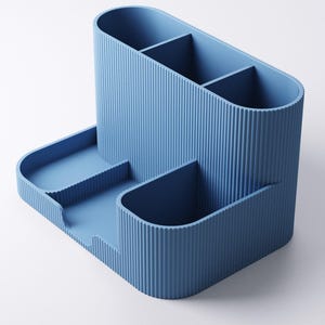 May include: A blue desk tidy with a ribbed texture. It has several compartments, including a tall section with dividers and a lower tray area. The design is modern and minimalist, suitable for office or home use.