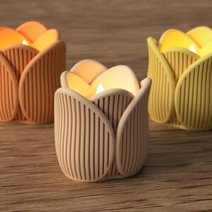 May include: Three tulip-shaped candle holders in shades of orange, beige, and yellow. Each holder has a vertical ribbed design and holds a lit candle, creating a warm glow. The candle holders are on a wooden surface.
