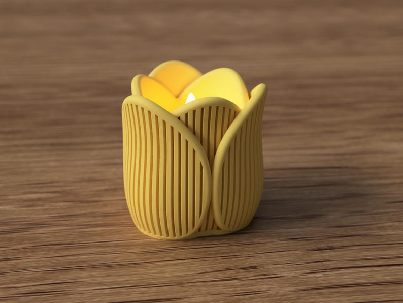 May include: A yellow tulip-shaped candle holder with a lit candle inside. The holder has vertical lines and a petal design. The candle holder is on a wooden surface.