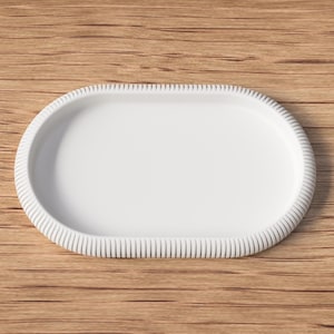 Puede incluir: Una bandeja blanca de forma ovalada con un borde texturizado y acanalado. La bandeja est&aacute; sobre un fondo de madera. Esta bandeja decorativa es adecuada para servir alimentos o exhibir objetos peque&ntilde;os.