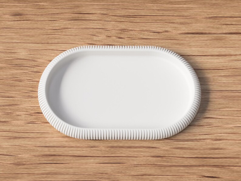 Puede incluir: Una bandeja blanca de forma ovalada con un borde texturizado y acanalado. La bandeja est&aacute; sobre un fondo de madera. Esta bandeja decorativa es adecuada para servir alimentos o exhibir objetos peque&ntilde;os.