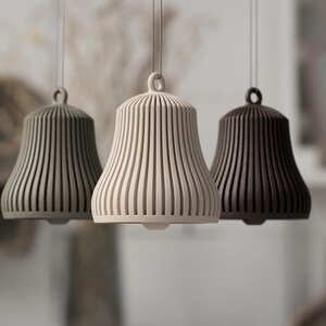 May include: Three pendant lights in a row, each with a bell-shaped shade. The shades are vertically ribbed and come in shades of green, cream, and brown. The lights hang from thin cords.