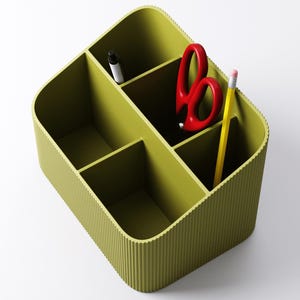 May include: A green desk organizer with multiple compartments. It contains a black pen, red scissors, and a yellow pencil with a pink eraser. The organizer has a ribbed exterior and is designed to hold office supplies.