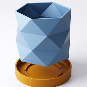 May include: A geometric blue planter with a faceted design, sitting on a round, mustard-yellow saucer. The planter has a hexagonal top and a modern, angular aesthetic. The planter and saucer are made of a solid material.