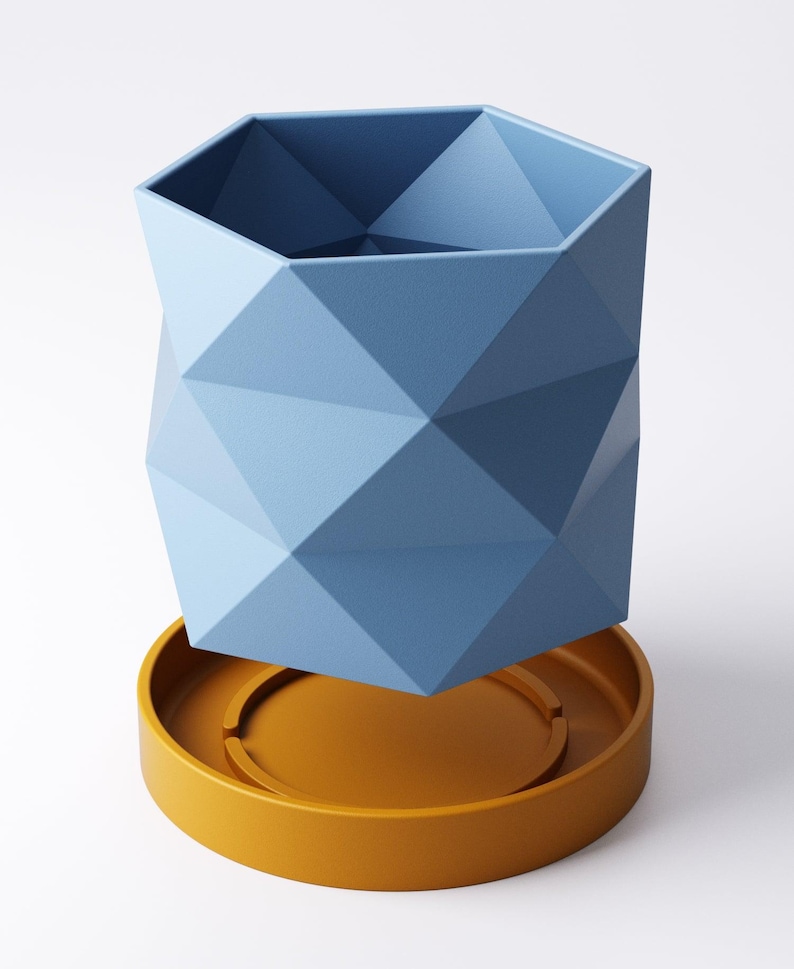 May include: A geometric blue planter with a faceted design, sitting on a round, mustard-yellow saucer. The planter has a hexagonal top and a modern, angular aesthetic. The planter and saucer are made of a solid material.