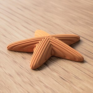 May include: A light brown, five-pointed starfish with textured ridges, resting on a wooden surface. The starfish is a decorative item, possibly for home decor or coastal-themed crafts.