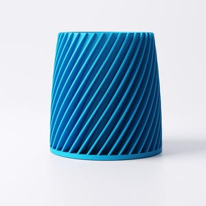K&ouml;nnte beinhalten: Ein leuchtend blauer zylindrischer Beh&auml;lter mit einem spiralf&ouml;rmigen Rippendesign. Der Beh&auml;lter hat einen festen Boden und eine leicht ausgestellte Oberseite. Die diagonalen Linien erzeugen einen dynamischen visuellen Effekt. Der Gegenstand steht vor einem schlichten wei&szlig;en Hintergrund.